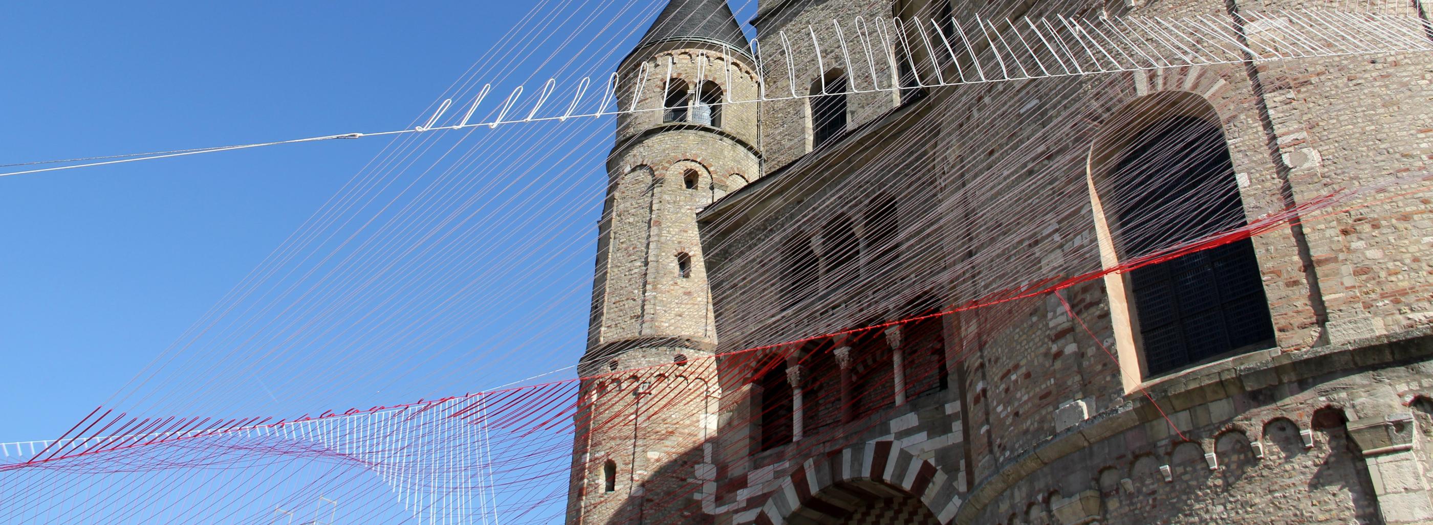 Blick von unten auf den Trierer Dom. Am Dom ist ein Netz vor den blauen Himmel gespannt