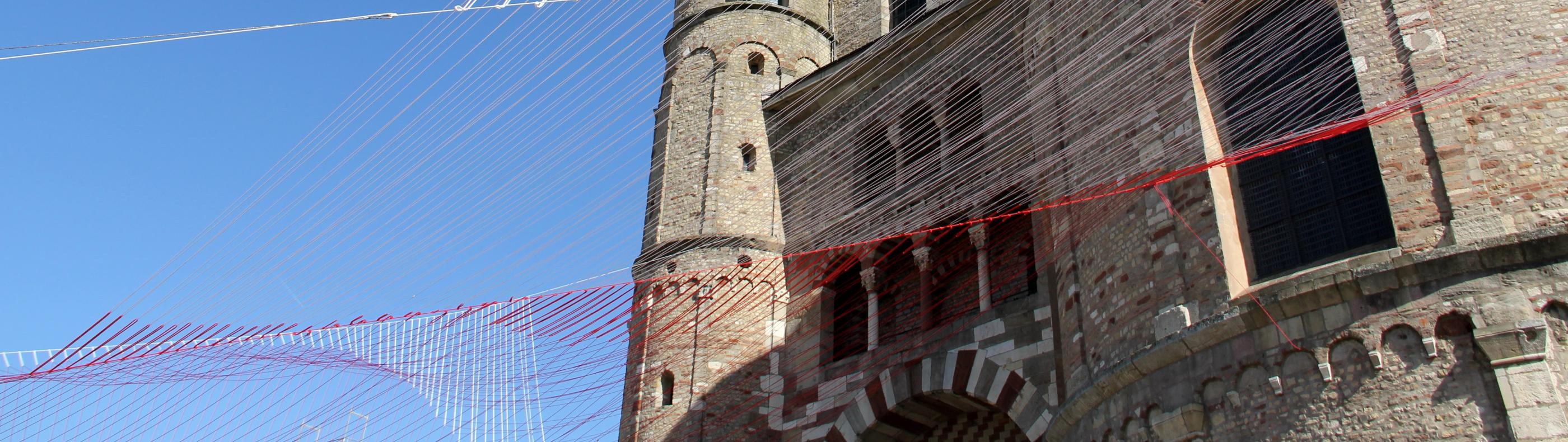 Blick von unten auf den Trierer Dom. Am Dom ist ein Netz vor den blauen Himmel gespannt