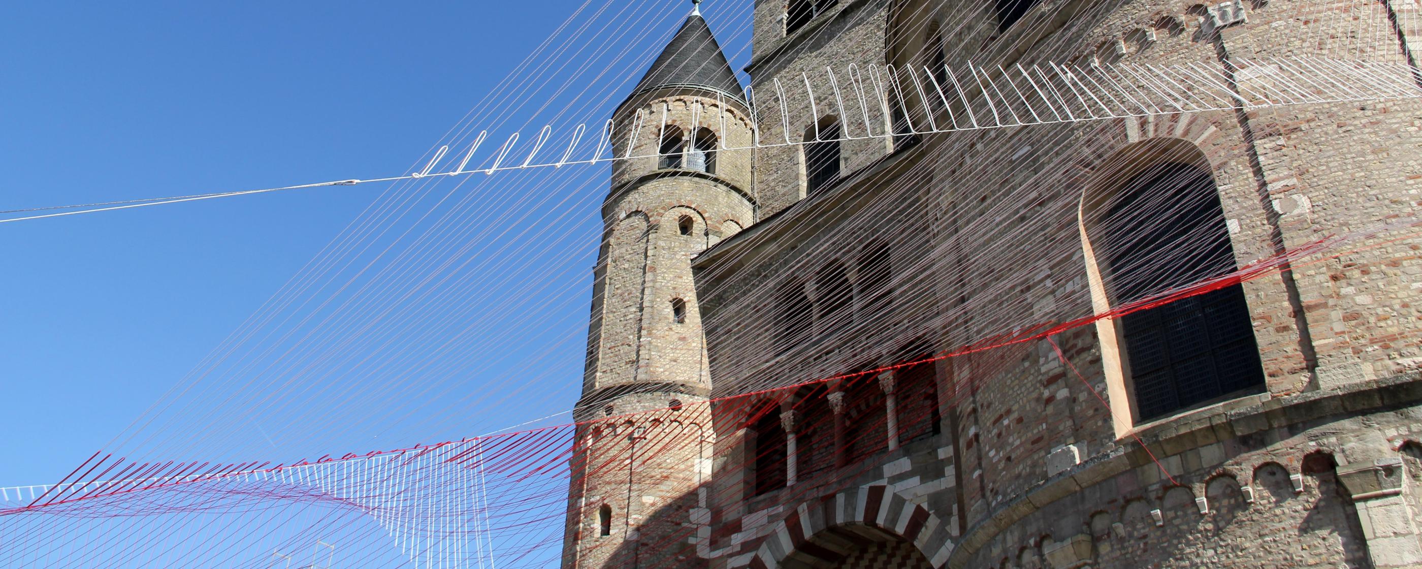 Blick von unten auf den Trierer Dom. Am Dom ist ein Netz vor den blauen Himmel gespannt