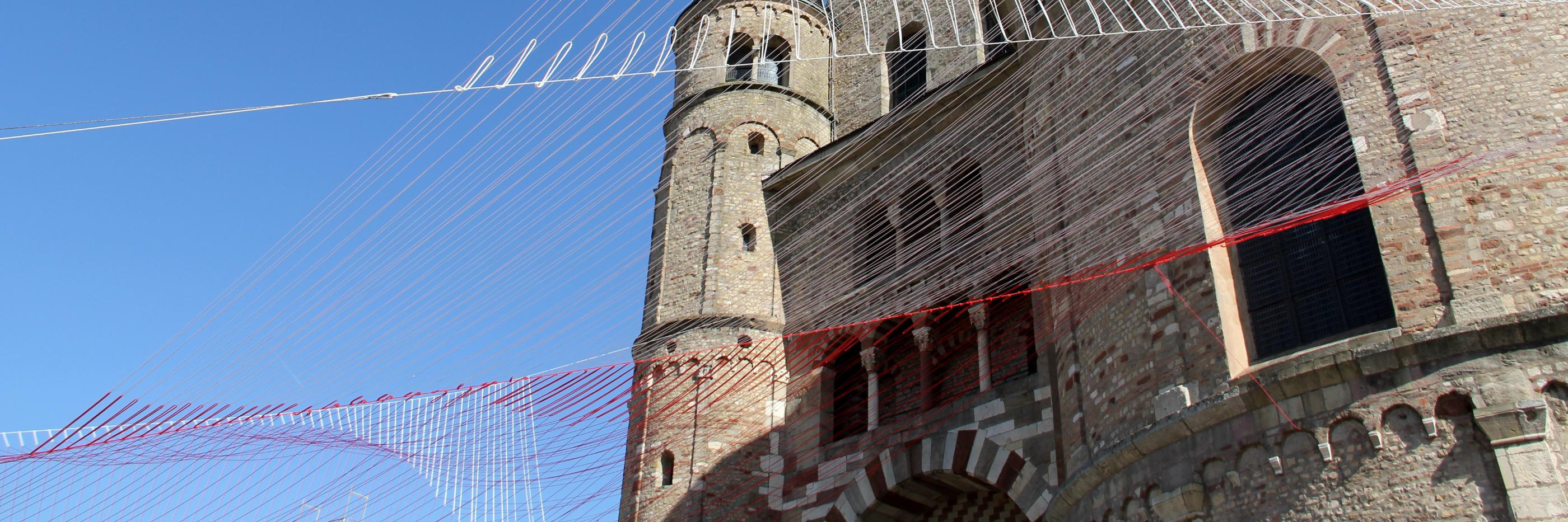 Blick von unten auf den Trierer Dom. Am Dom ist ein Netz vor den blauen Himmel gespannt