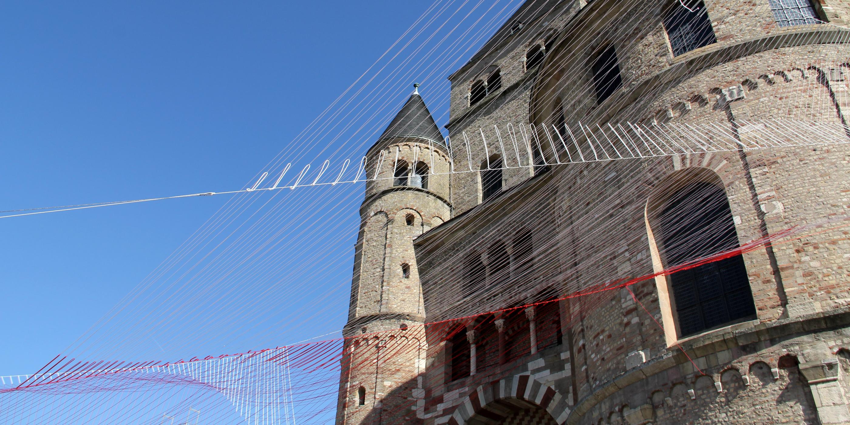 Blick von unten auf den Trierer Dom. Am Dom ist ein Netz vor den blauen Himmel gespannt