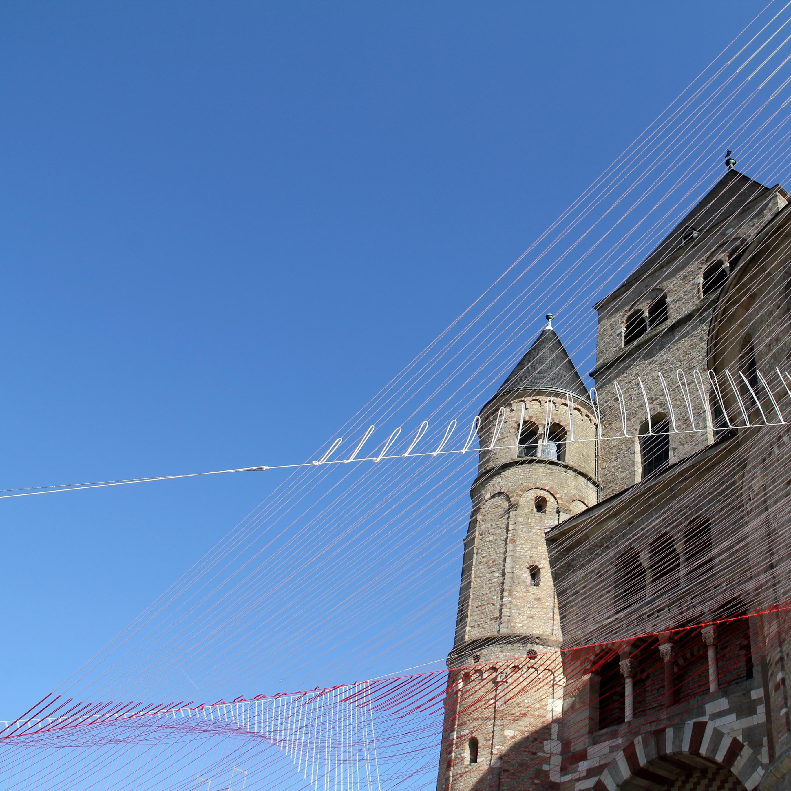 Blick von unten auf den Trierer Dom. Am Dom ist ein Netz vor den blauen Himmel gespannt