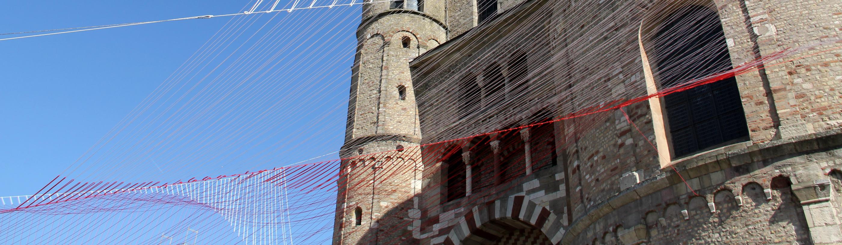 Blick von unten auf den Trierer Dom. Am Dom ist ein Netz vor den blauen Himmel gespannt