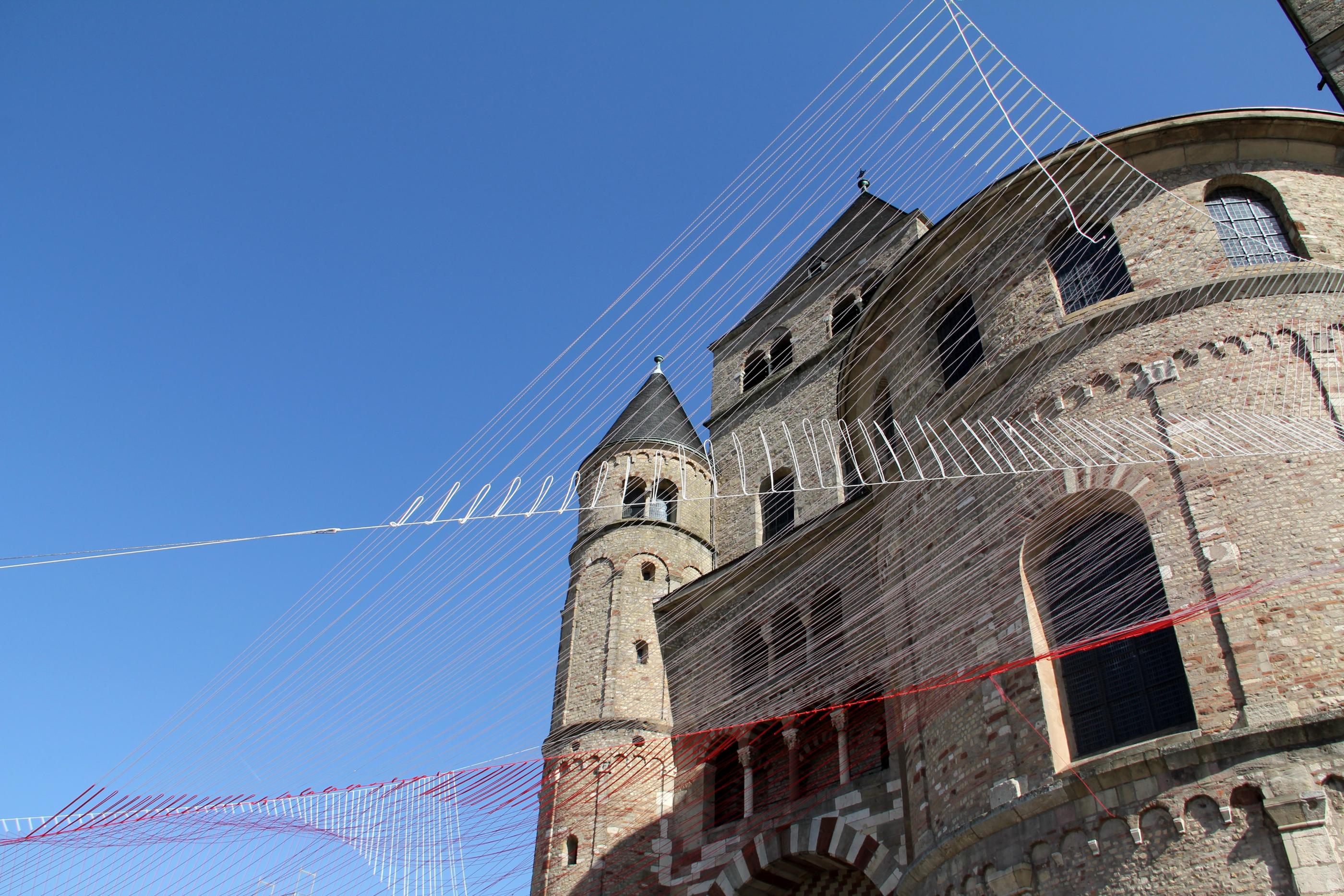 Blick von unten auf den Trierer Dom. Am Dom ist ein Netz vor den blauen Himmel gespannt