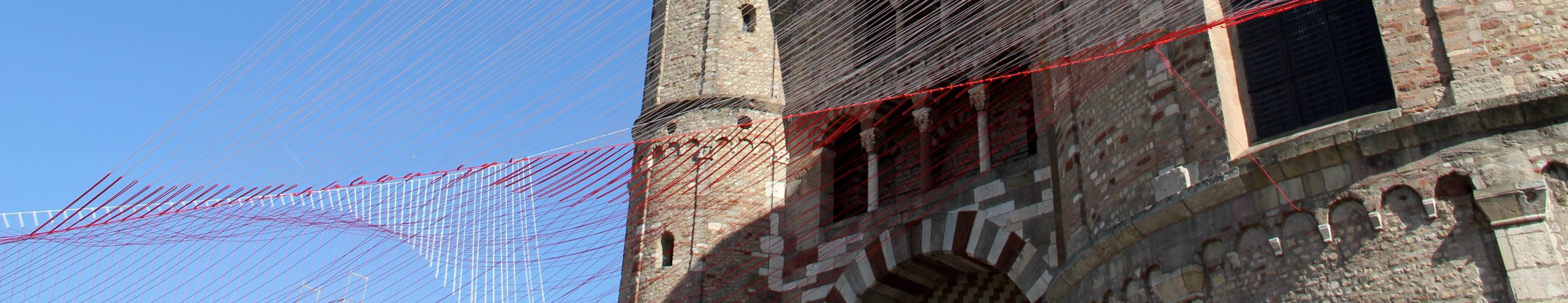 Blick von unten auf den Trierer Dom. Am Dom ist ein Netz vor den blauen Himmel gespannt
